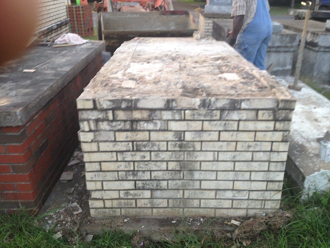 An old white-brick tomb, cracked and stained, during demolition.