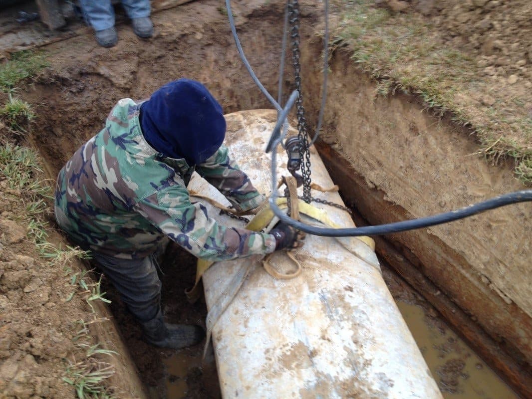 A worker standing in an opened grave, rigging straps around a vault for lifting.