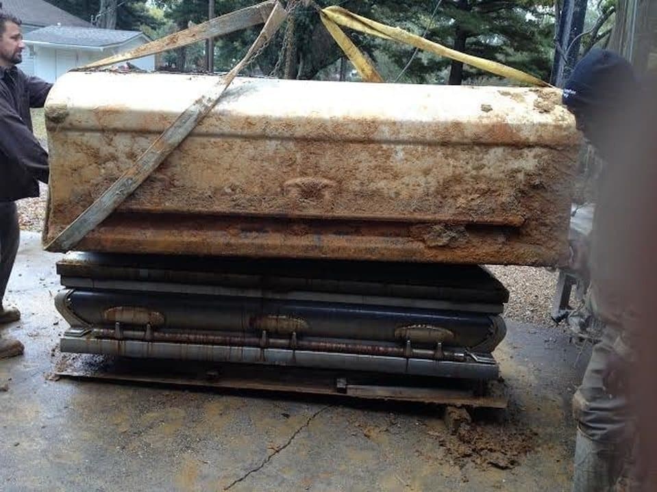 A vault and casket lifted out of the ground on straps during a disinterment.