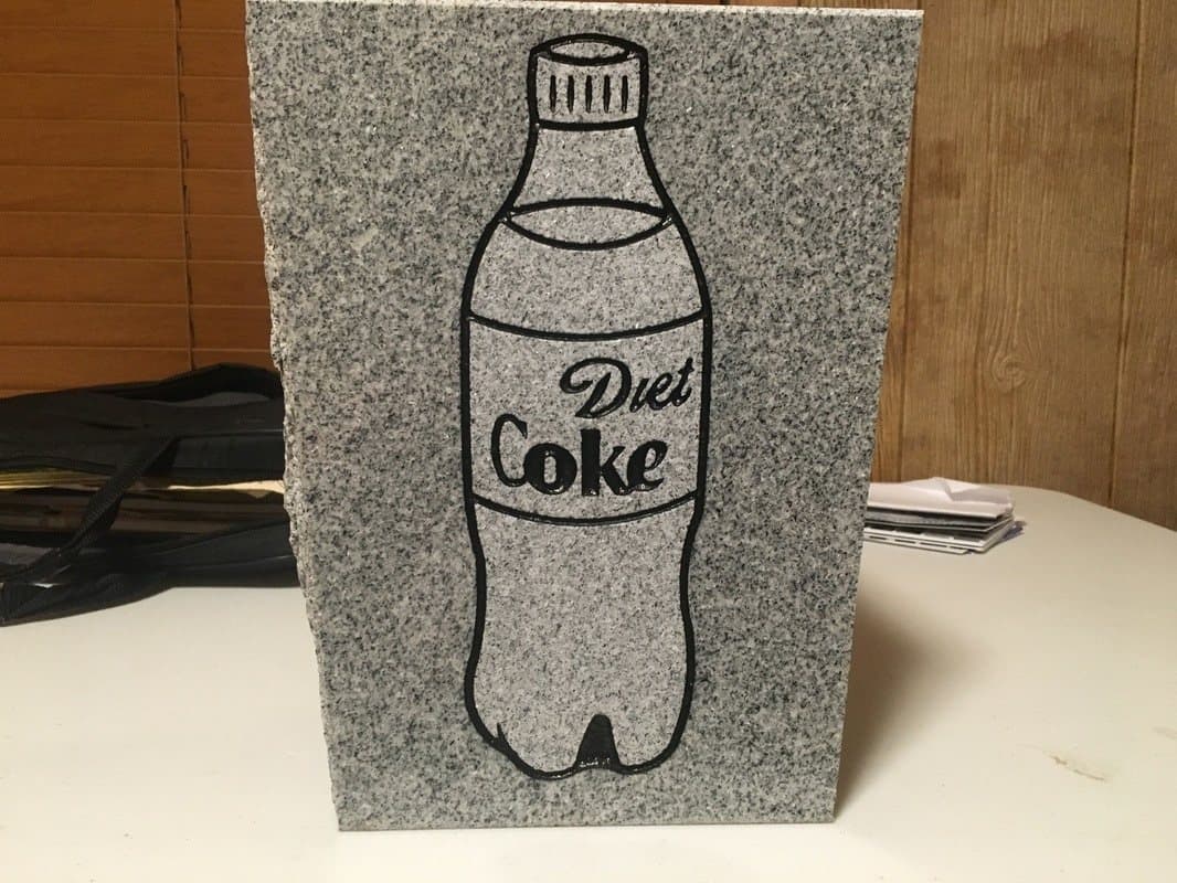 A gray granite stone etched with the outline of a soda bottle.