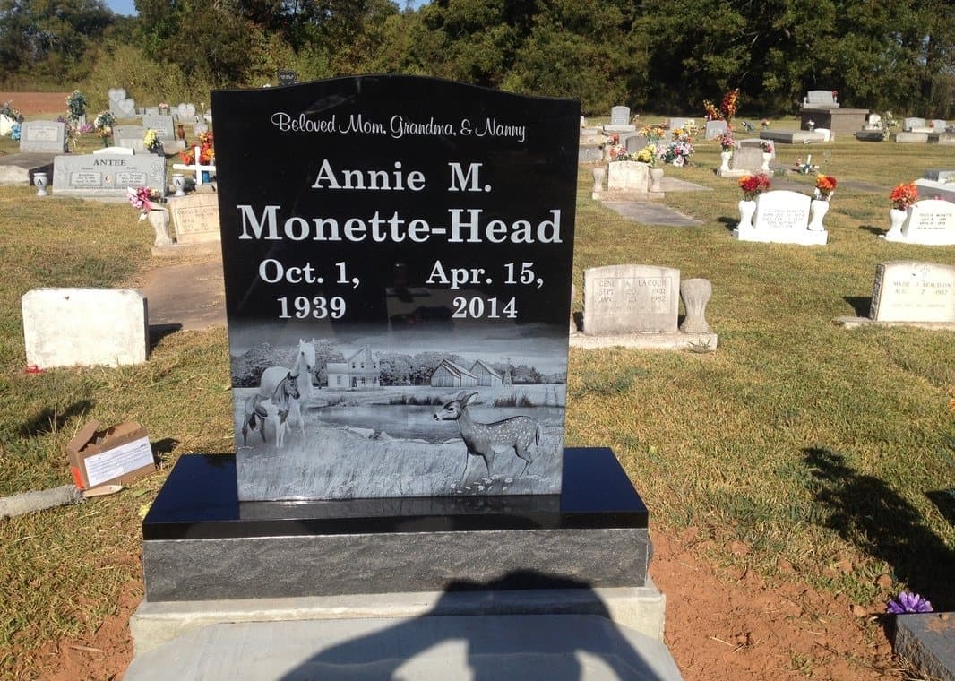 A black granite upright etched with a country landscape beneath the name and dates.