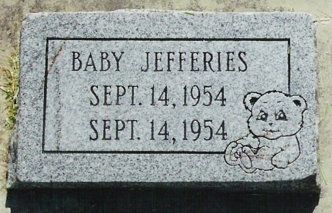 A flat gray granite marker for an infant, engraved with a teddy bear.