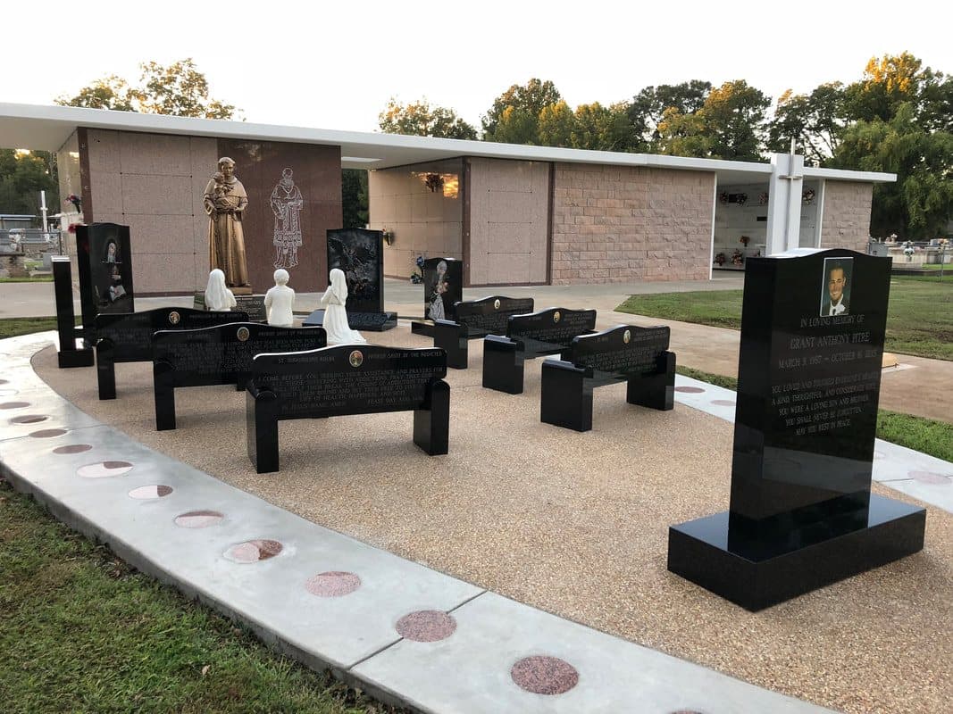A prayer garden of black granite benches, statues, and monuments beside a church building.