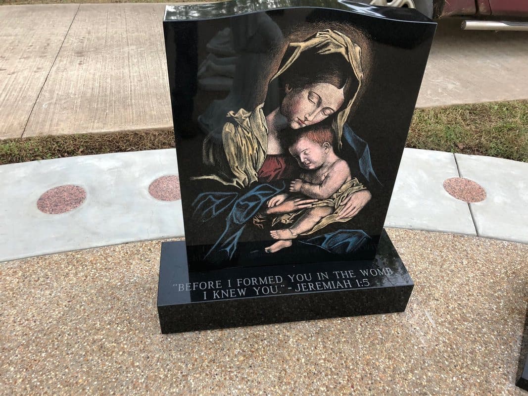 A black granite monument etched in color with the Virgin Mary holding the Christ Child.