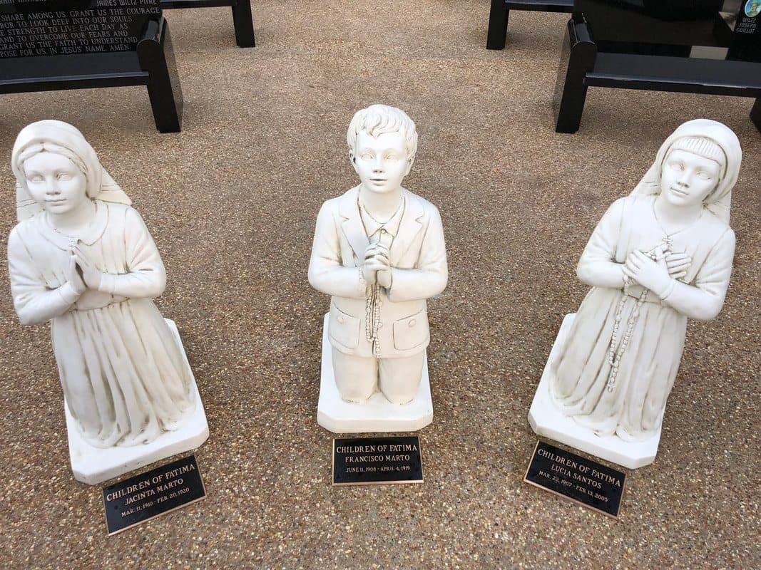 White statues of three children kneeling in prayer, each with a small bronze plaque.