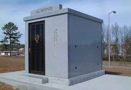 A gray granite private mausoleum with a dark door and the family name across the top.