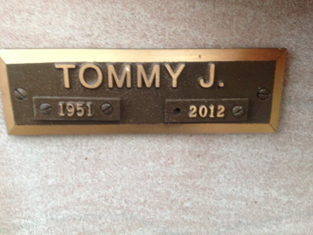 A small cast bronze nameplate with a first name and the years 1951 and 2012.