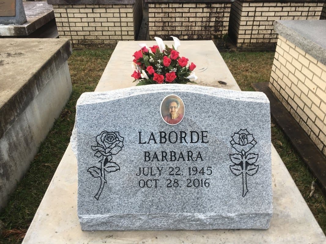 A gray granite slant headstone with carved roses and an oval porcelain portrait, set on a concrete vault.