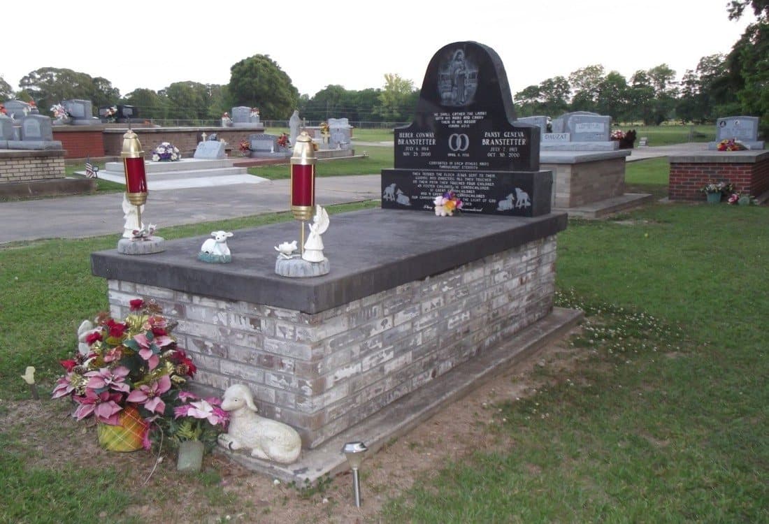 A charcoal-gray brick tomb with a black granite upright headstone and flowers.