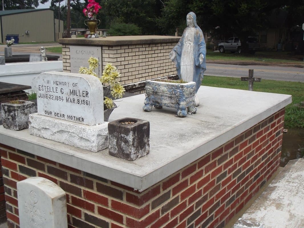 A red brick tomb with a white concrete top and a statue of the Virgin Mary.