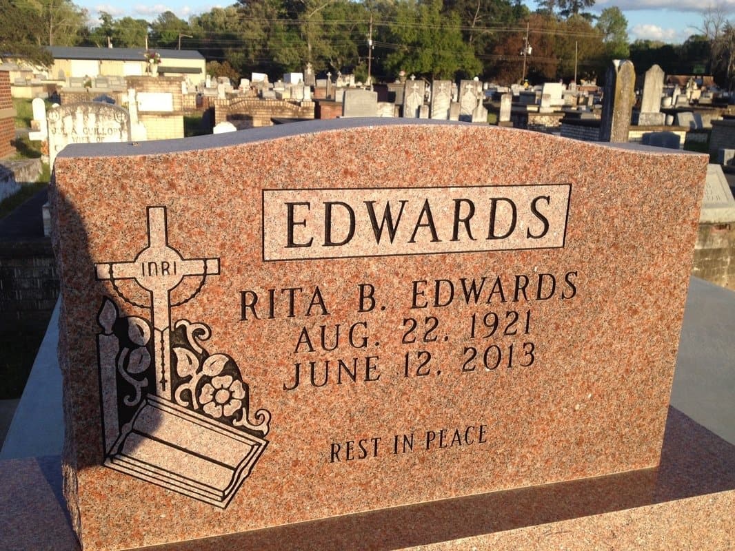 A red granite upright headstone carved with a cross and flowers.