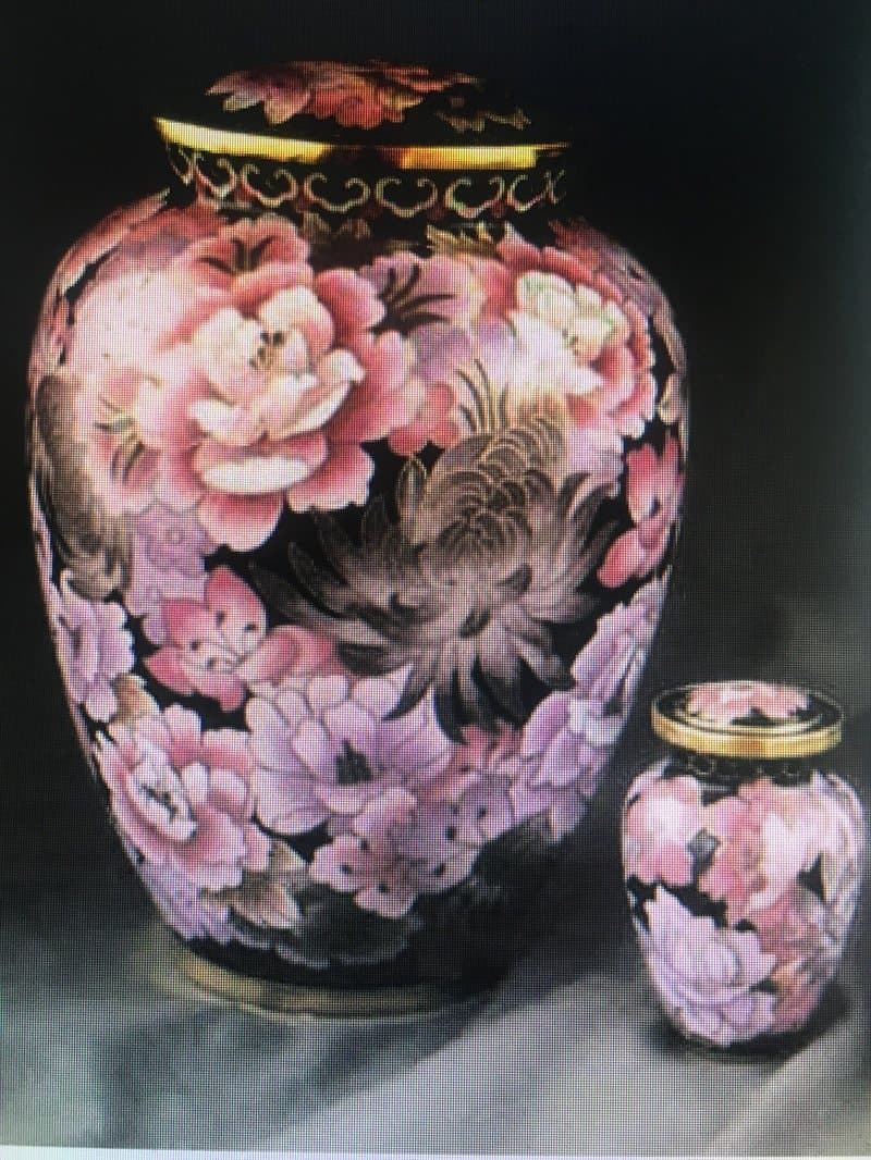 A cremation urn covered in pink peonies, beside a matching keepsake urn.