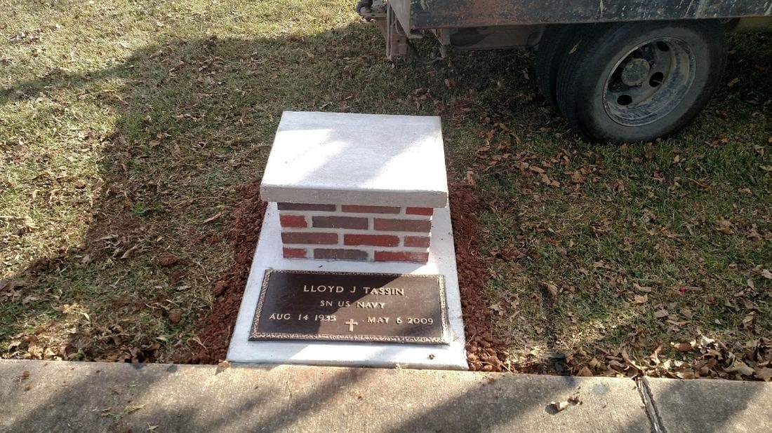 A small red brick cremation urn vault with a white top and a bronze plaque.