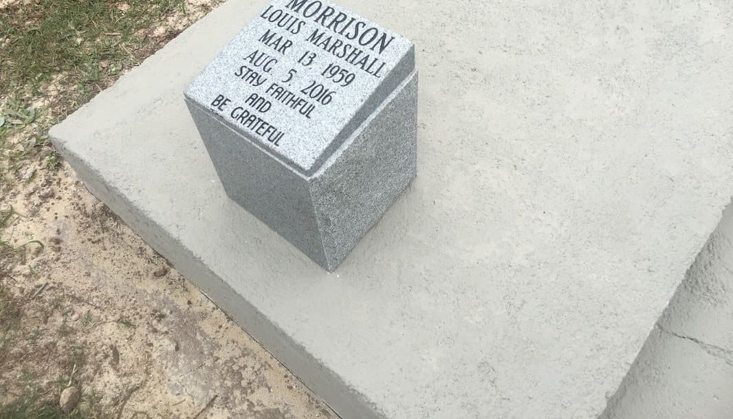 A single gray granite urn vault engraved with a name and dates, on a concrete pad.