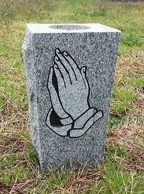 A gray granite vase etched with praying hands.