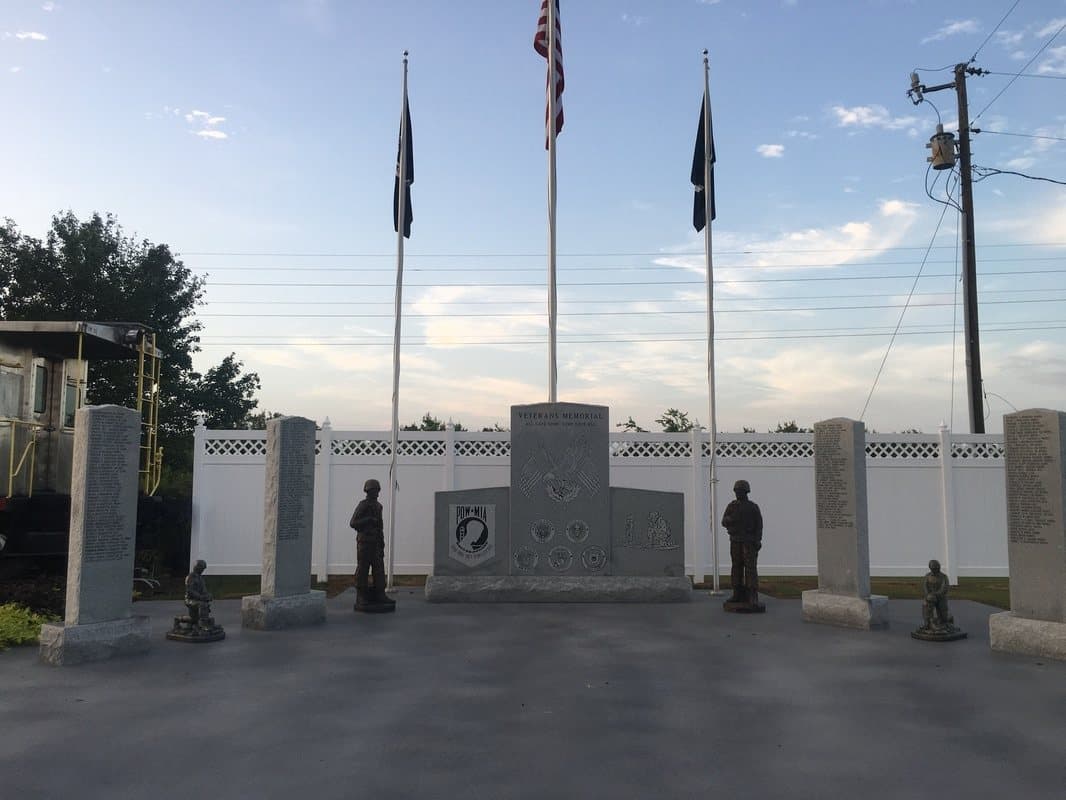A veterans memorial with three flagpoles and statues of soldiers, at dusk.
