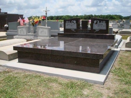 A dark granite ledger and wrap covering a double grave, with headstones behind it.