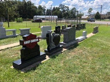 Custom black granite monuments at the Marksville yard, one shaped like a motorcycle company emblem.