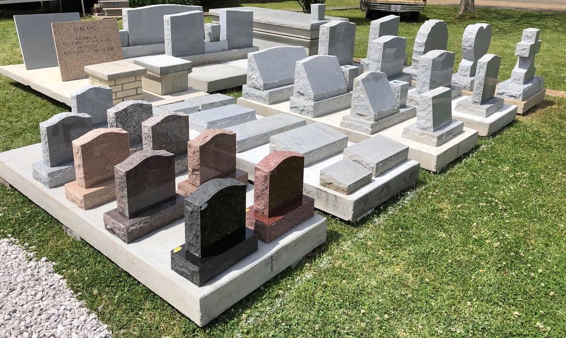 Rows of headstone samples in gray, pink, red, and black granite on concrete pads at the Marksville yard.
